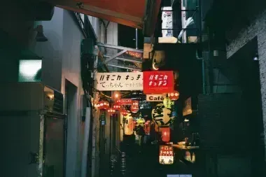 Small street with lit cafe and shop signs above at night